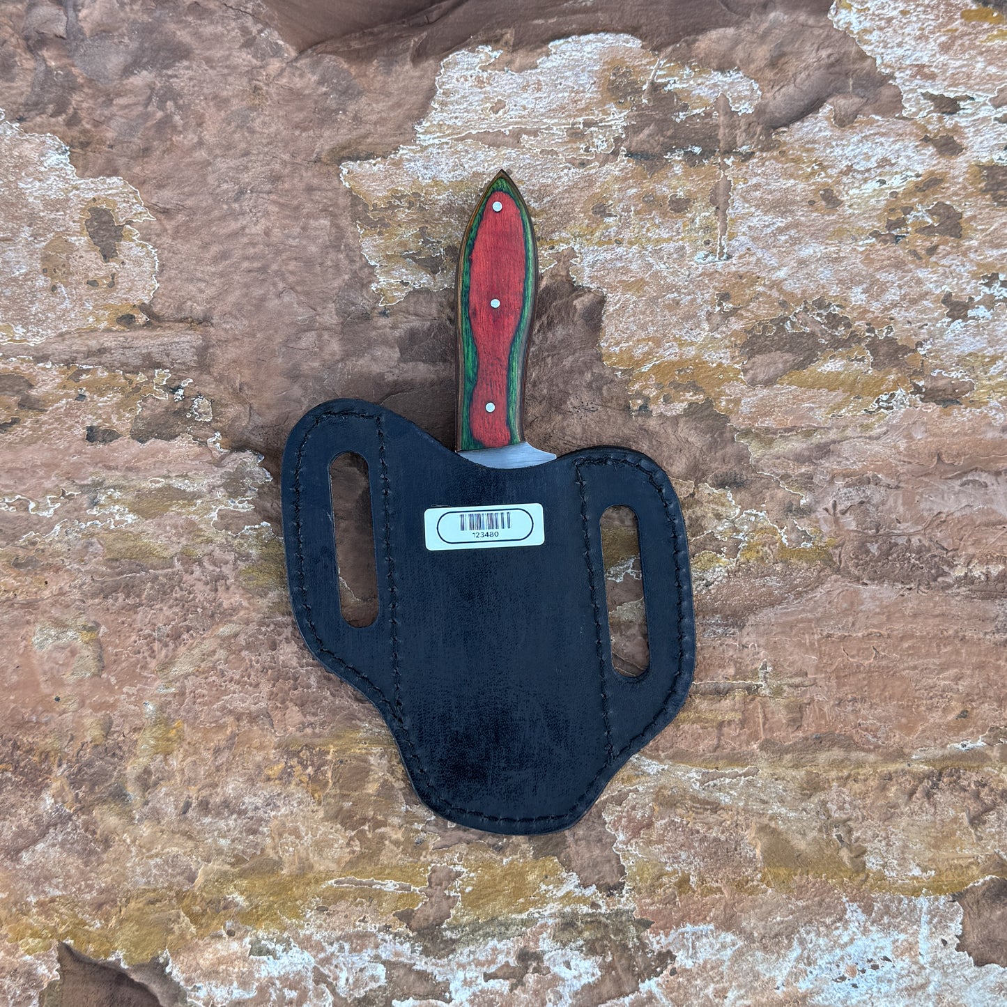 A full-tang fixed-blade knife made from 1095 high-carbon steel with a contoured red dyed-wood handle featuring rich grain patterns, shown with its hand-stitched brown leather sheath. Crafted by Blue Spade Forge for hunting, camping, carving, and rugged outdoor use.