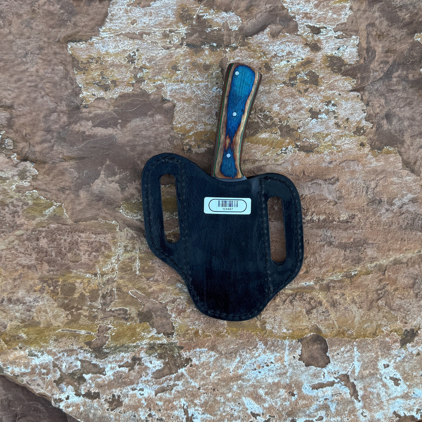 A full-tang 1095 high-carbon steel field knife with a contoured dyed-wood handle featuring bold color and rich grain patterns, shown with its hand-stitched brown leather sheath. Crafted by Blue Spade Forge for field use, camping, bushcraft, and rugged outdoor tasks