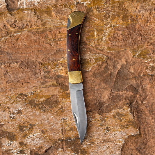 Ironclad Rose Folder folding knife with rosewood handle and brass bolsters on rock background