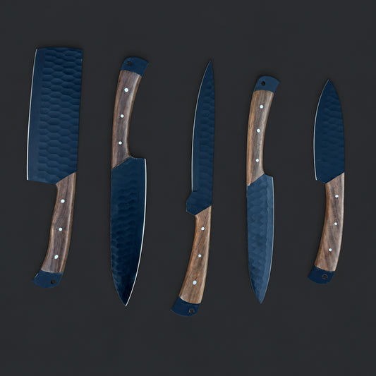 “A 5-piece chef knife set featuring matte black textured blades and dark hardwood handles displayed on natural stone. Includes a paring knife, utility knife, slicer, chef knife, and cleaver.