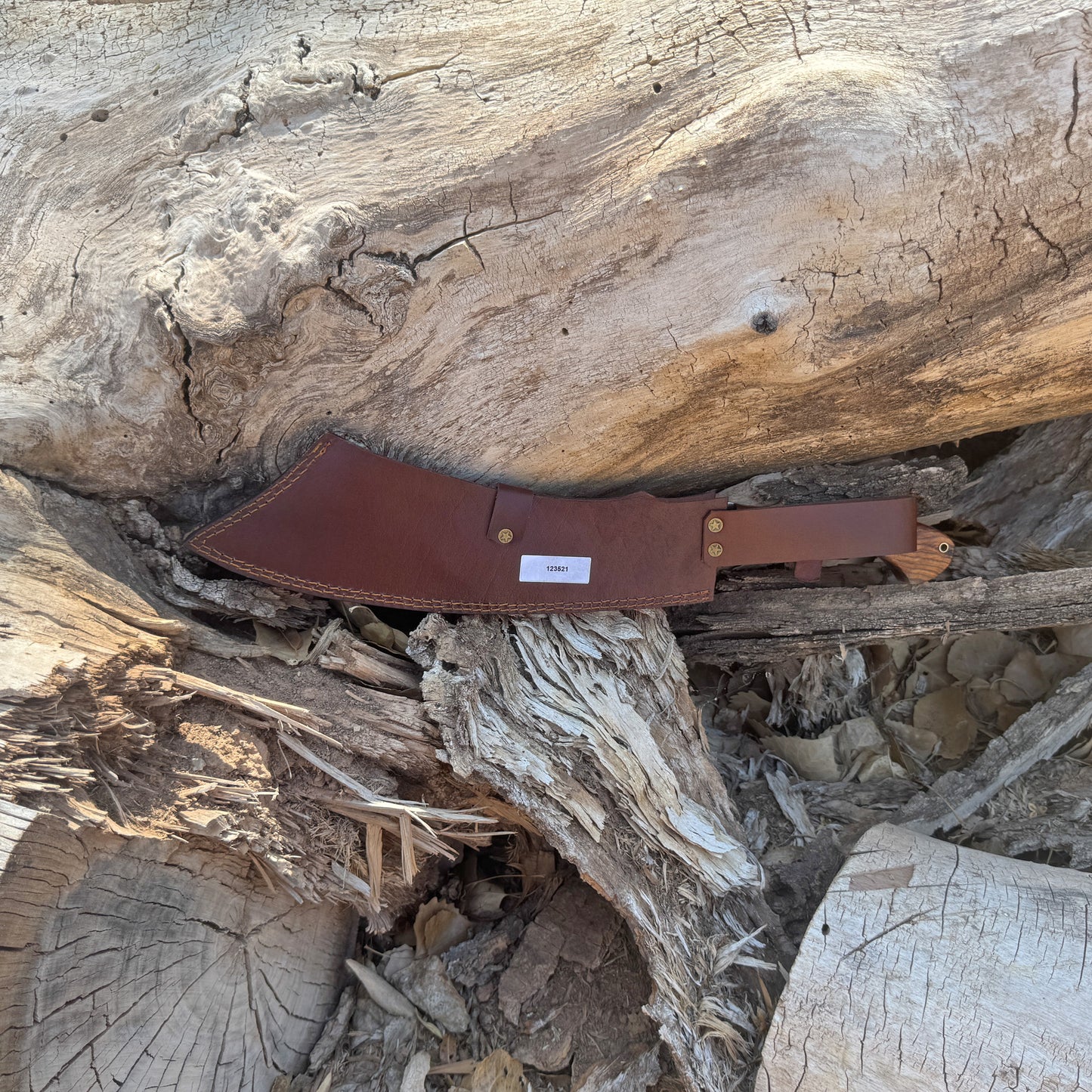 The Dreadfang machete featuring a hand-forged clip-point blade with a smooth walnut handle, displayed outdoors on a natural wooden surface to highlight its chopping power, precise piercing profile, rugged full-tang construction, and handcrafted Blue Spade Forge quality built for brush clearing and camp work.