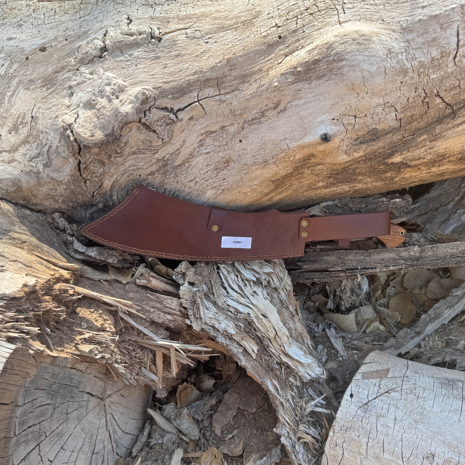 The Dreadfang machete featuring a hand-forged clip-point blade with a smooth walnut handle, displayed outdoors on a natural wooden surface to highlight its chopping power, precise piercing profile, rugged full-tang construction, and handcrafted Blue Spade Forge quality built for brush clearing and camp work.