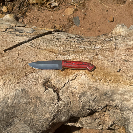 Bloodwood Scout fixed blade knife with red dyed-wood handle

High-carbon blade displayed on brown leather sheath

Close-up of deep red wood handle with visible grain

Bloodwood Scout knife on natural wood background

Knife and hand-stitched leather sheath arranged together

Outdoor fixed blade knife in natural lighting

Blue Spade Forge Bloodwood Scout held in hand for scale

Rugged field knife ready for hunting and bushcraft tasks