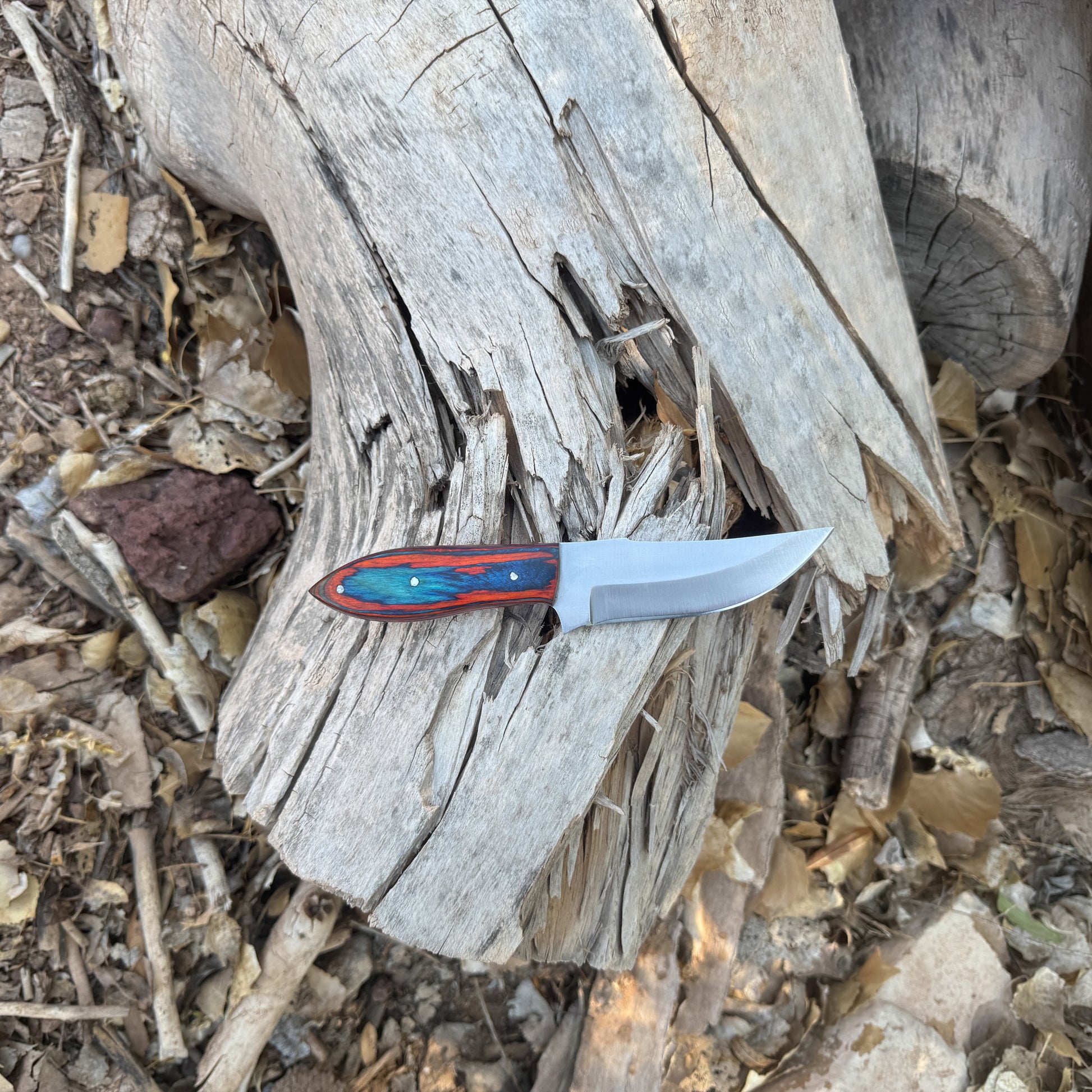 Blaze Creek Bowie knife with multi-tone wood handle

Full-tang clip-point blade displayed on leather sheath

Close-up of blue, green, and reddish handle grain

Bowie knife shown on natural wood surface

Blaze Creek knife and hand-stitched sheath arranged together

Outdoor Bowie knife in natural lighting

Blue Spade Forge Blaze Creek held in hand for scale

Clip-point blade and multi-tone handle product display