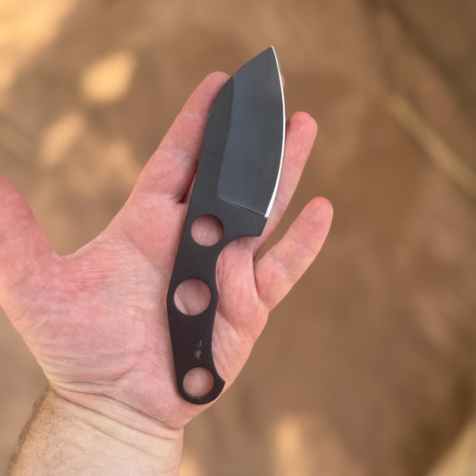 The Black Talon skeleton knife featuring a hand-forged high-carbon-steel blade with a black protective finish and a lightweight skeletonized full-tang handle, displayed beside its hand-stitched, custom hand-tooled leather pancake sheath on a rugged rock and moss landscape, showcasing its compact everyday-carry design, minimalist construction, and durable craftsmanship for trail, ranch, and utility use.