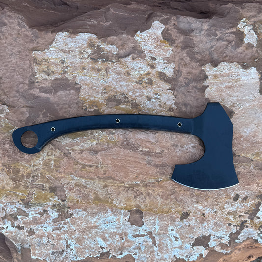 A full-tang blackout tactical axe forged from 5160 spring steel with a curved black micarta handle, photographed on natural desert stone. Designed for chopping, bushcraft, camping, and rugged field work