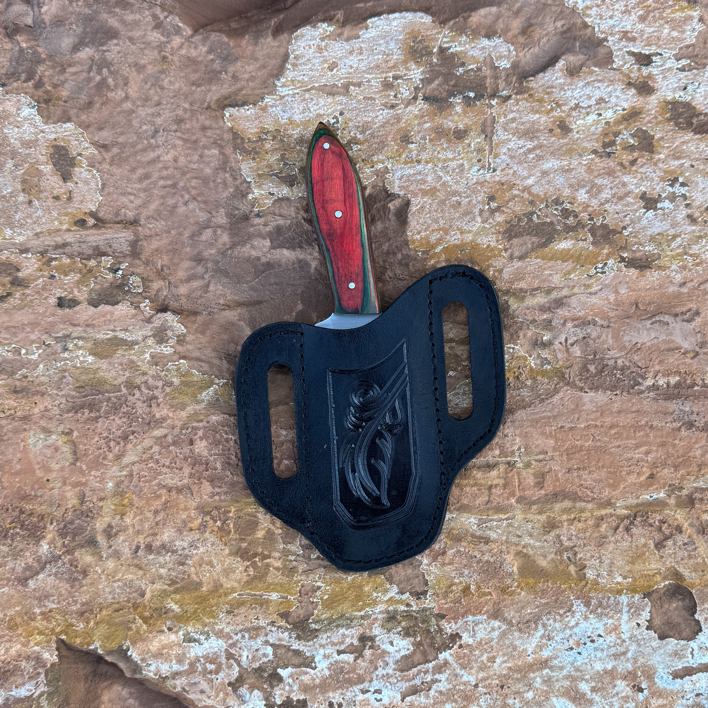 A full-tang fixed-blade knife made from 1095 high-carbon steel with a contoured red dyed-wood handle featuring rich grain patterns, shown with its hand-stitched brown leather sheath. Crafted by Blue Spade Forge for hunting, camping, carving, and rugged outdoor use.