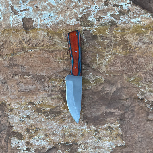 A full-tang drop-point field knife with a satin-finished blade and a richly grained hardwood handle, shown beside a hand-stitched leather sheath. Crafted by Blue Spade Forge for hunting, camping, carving, and rugged outdoor field use.