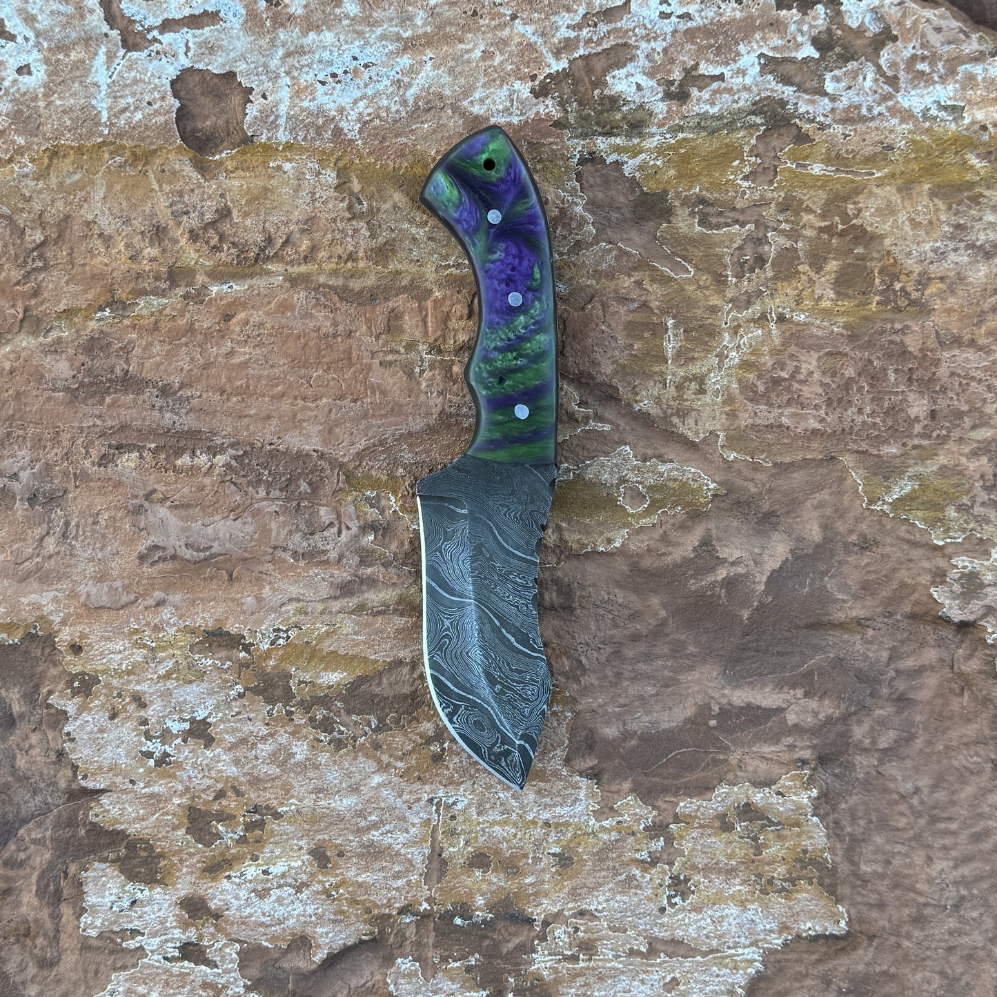 Vortex Fang Damascus fixed blade knife with swirling resin handle

Close-up of patterned Damascus blade with wave design

Resin-cast handle with multicolor swirl detail

Vortex Fang knife displayed on brown leather sheath

Knife and sheath arranged on natural wood background

Outdoor knife with resin handle in natural lighting

Blue Spade Forge Vortex Fang held in hand for size reference

Damascus blade and resin handle close-up product showcase