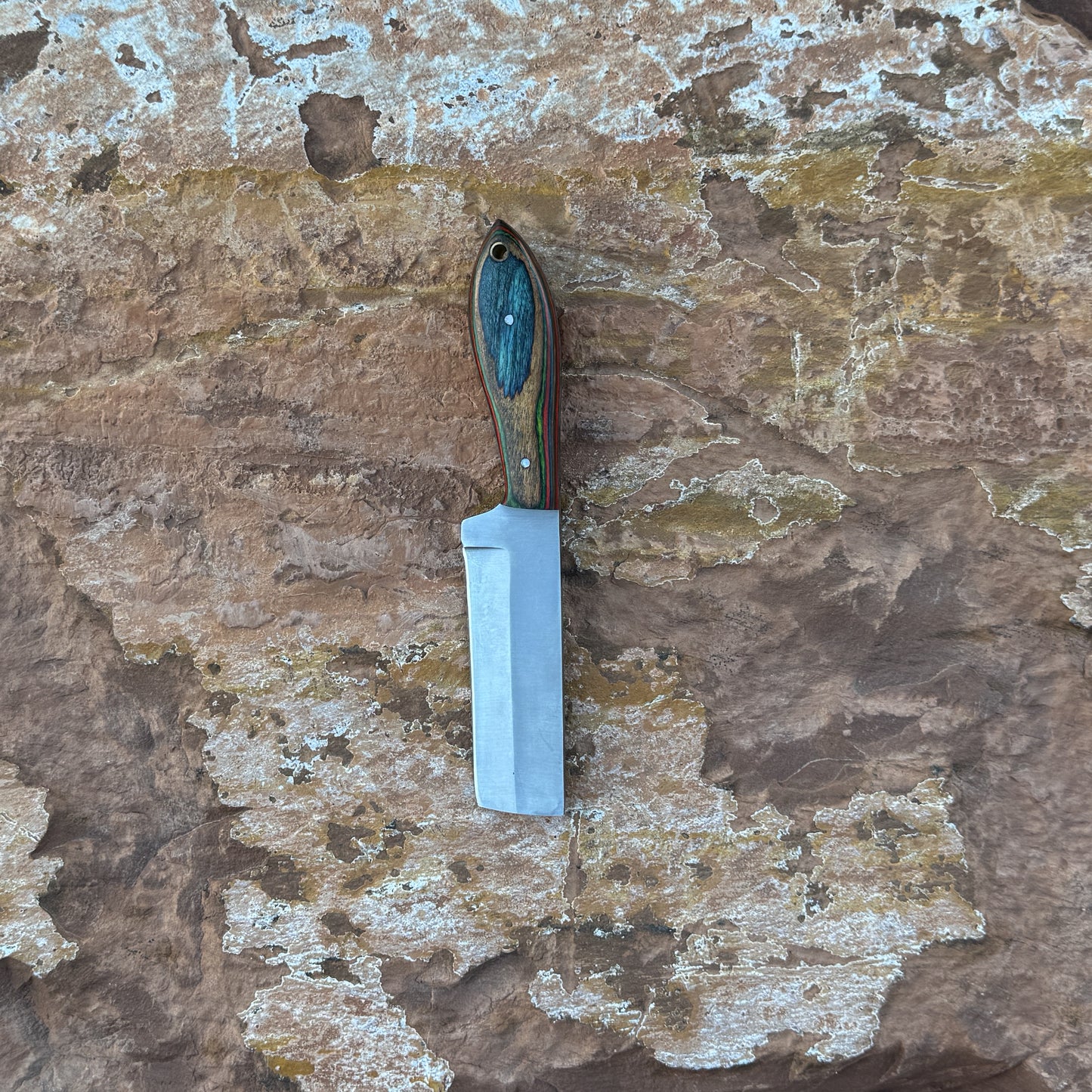 Ridge Cowboy knife with squared cowboy-style blade

Compact cowboy knife displayed on hand-stitched leather sheath

Close-up of multi-tone hardwood handle grain

Ridge Cowboy knife on natural wood background

Knife and leather sheath arranged for product display

Outdoor cowboy-style knife in natural lighting

Blue Spade Forge Ridge Cowboy held in hand for scale

Detail shot of squared blade and multi-tone handle