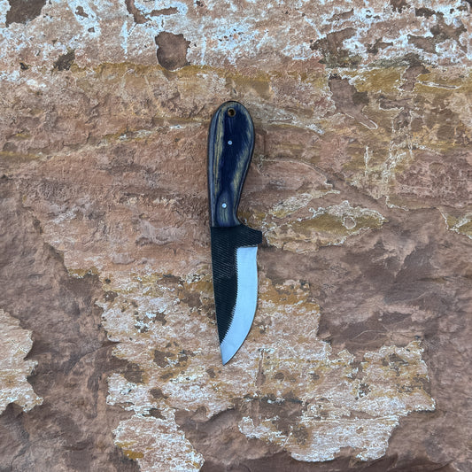 Shadow Rasp Hunter knife with rasp-textured blade

Curved high-carbon steel blade on leather sheath

Dark hardwood handle with rivets close-up

Shadow Rasp Hunter displayed on natural wood background

Knife and hand-stitched sheath arranged for product showcase

Outdoor fixed blade knife in natural lighting

Blue Spade Forge Shadow Rasp Hunter held in hand for scale

Rasp-spine blade and hardwood handle detail shot