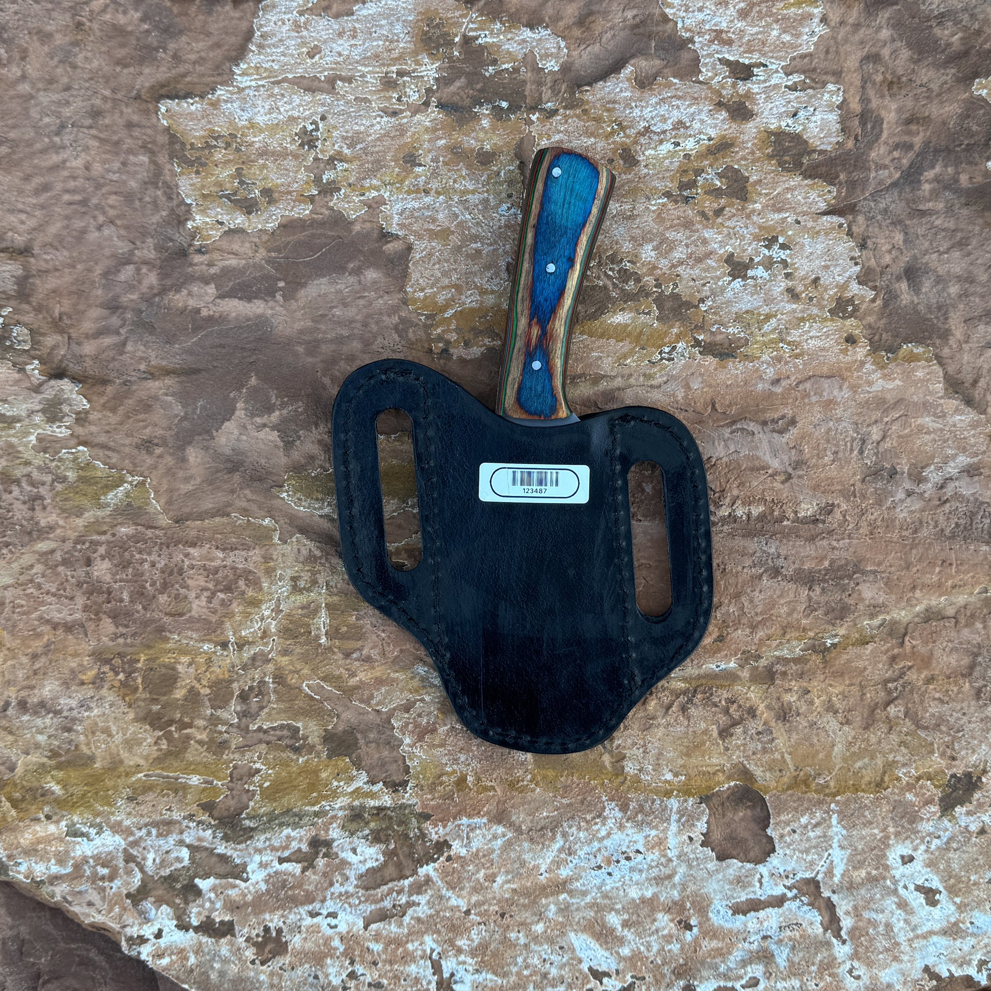 A full-tang 1095 high-carbon steel field knife with a contoured dyed-wood handle featuring bold color and rich grain patterns, shown with its hand-stitched brown leather sheath. Crafted by Blue Spade Forge for field use, camping, bushcraft, and rugged outdoor tasks