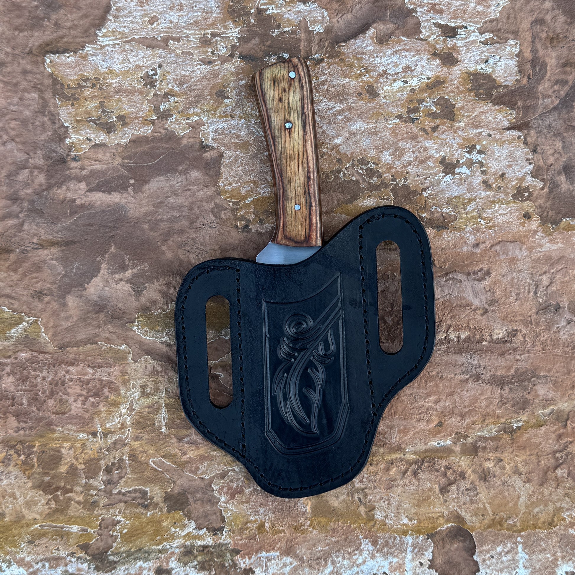 A straight-back fixed blade knife with a stainless-steel blade and contoured natural-wood handle, shown with its hand-stitched brown leather sheath. Designed by Blue Spade Forge for bushcraft, hunting, and versatile outdoor field use.