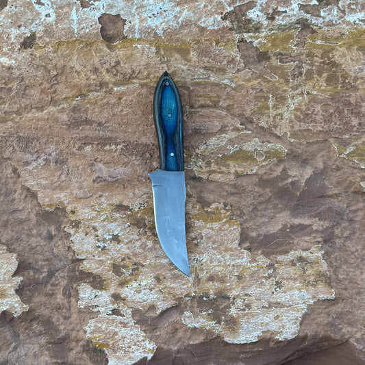 A full-tang upswept hunting knife with a satin-finished blade and deep-blue hardwood handle, reinforced with triple rivets. Shown alongside its hand-stitched leather sheath, crafted by Blue Spade Forge for field work, hunting, and rugged outdoor use.