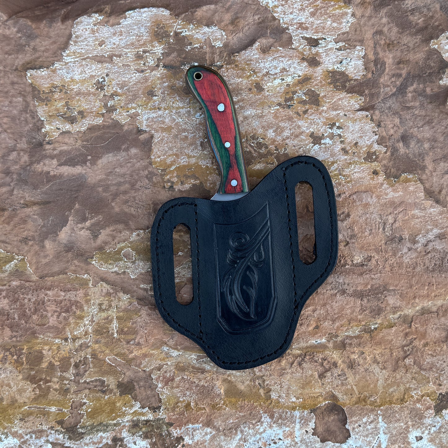 A full-tang stainless-steel field knife with a dyed-wood handle featuring rich grain patterns and vibrant coloration, shown with its handmade leather sheath. Designed by Blue Spade Forge for outdoor use, camping, and field tasks.