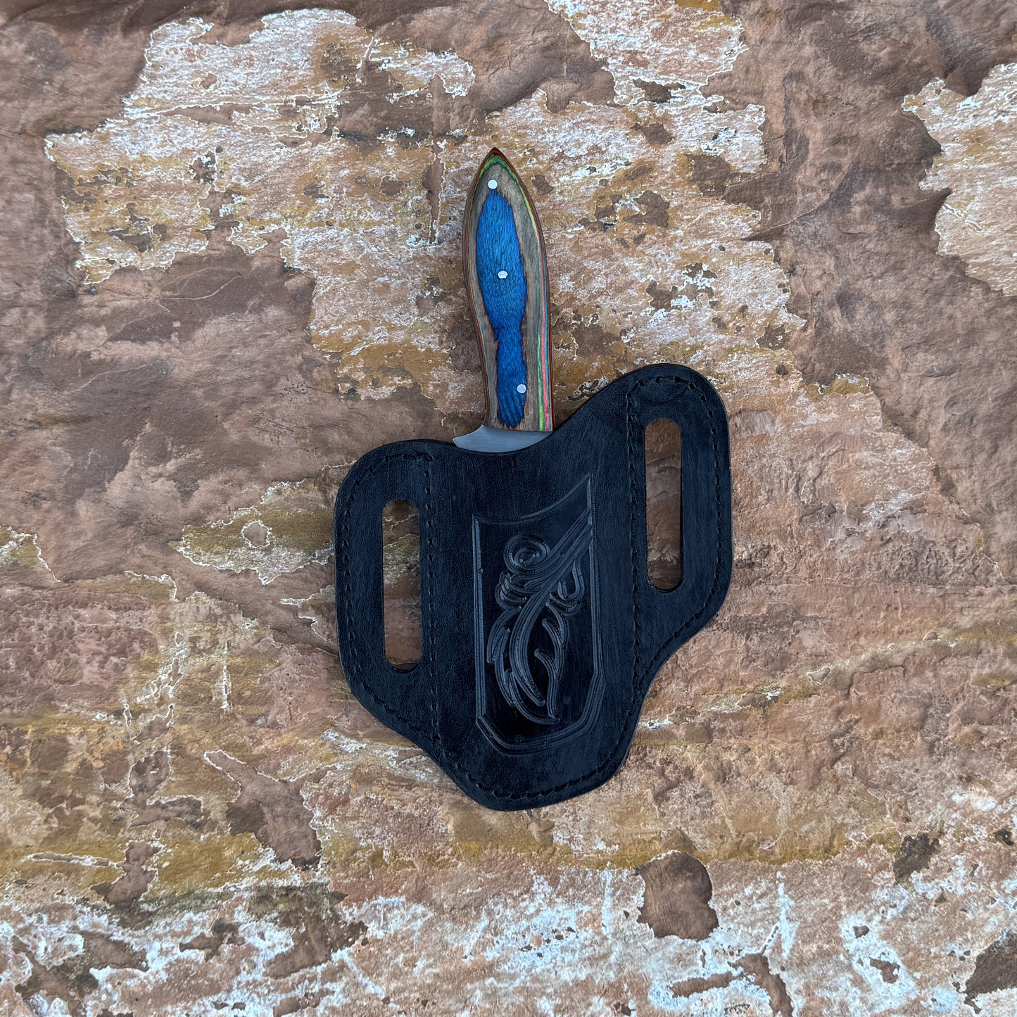 Blue Ridge Skinner knife with multi-tone hardwood handle

Sweeping clip-point blade displayed on leather sheath

Close-up of layered blue, red, green, and natural wood grain

Blue Ridge Skinner on natural wood background

Knife and hand-stitched leather sheath arranged together

Outdoor skinner knife in natural lighting

Blue Spade Forge Blue Ridge Skinner held in hand for scale

Detailed shot of clip-point blade and triple-riveted handle