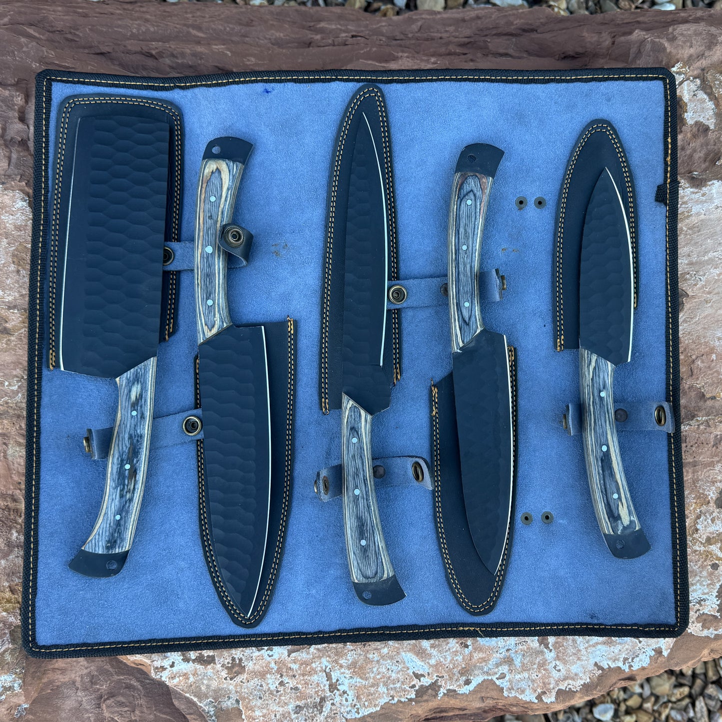 Five handcrafted high-carbon chef knives displayed in a premium leather knife roll.