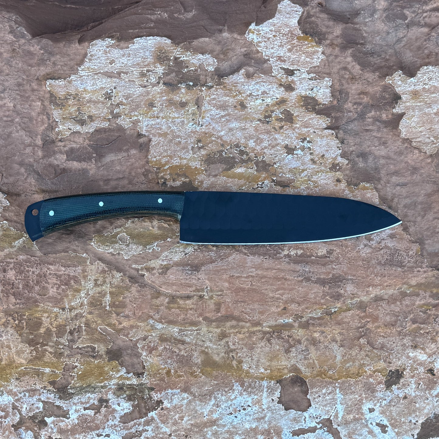 5160 high-carbon chef knife with black powder-coated blade, razor-sharp cutting edge, contoured micarta handle, and balanced profile designed for slicing, chopping, and professional kitchen use, shown unsheathed on textured stone surface