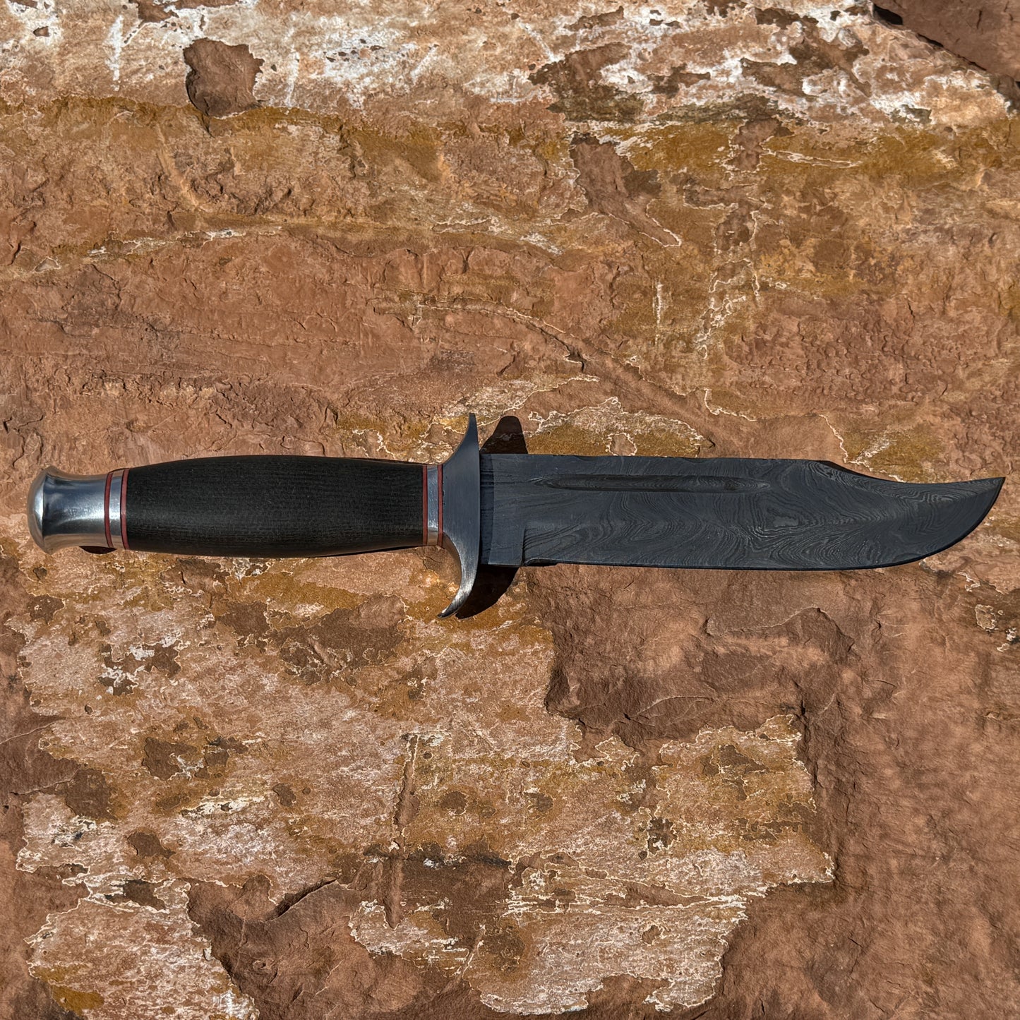 Iron Talon Bowie knife by Blue Spade Forge with Damascus steel blade and micarta handle displayed on rock outdoors