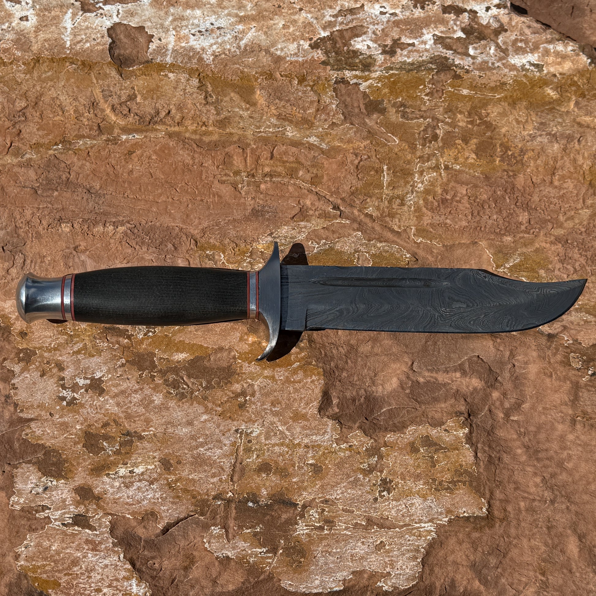 Iron Talon Bowie knife by Blue Spade Forge with Damascus steel blade and micarta handle displayed on rock outdoors