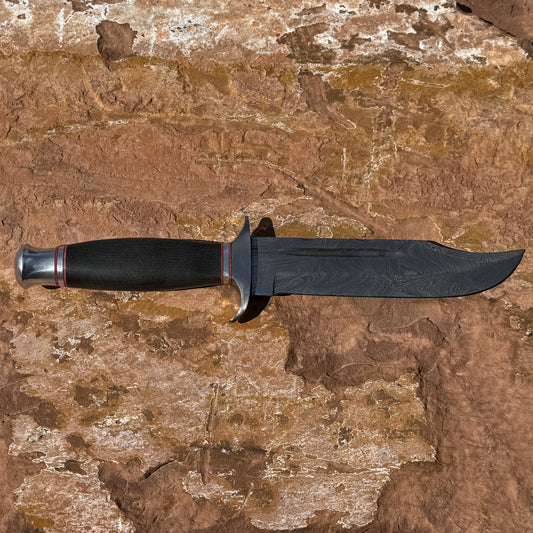 Iron Talon Bowie knife by Blue Spade Forge with Damascus steel blade and micarta handle displayed on rock outdoors