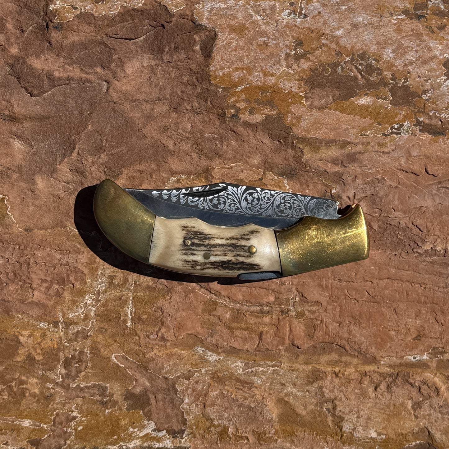 Ironclad Stag Fang Folder 1095 steel folding knife with laser etched blade, stag handle, and brass bolsters displayed on rock background