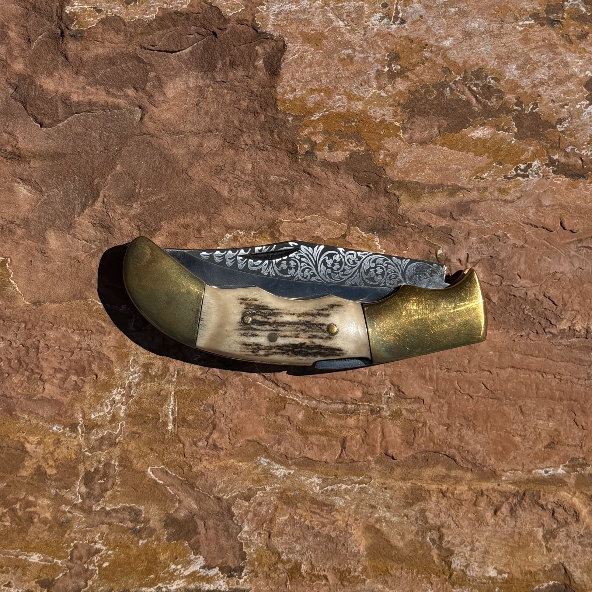 Ironclad Stag Fang Folder 1095 steel folding knife with laser etched blade, stag handle, and brass bolsters displayed on rock background
