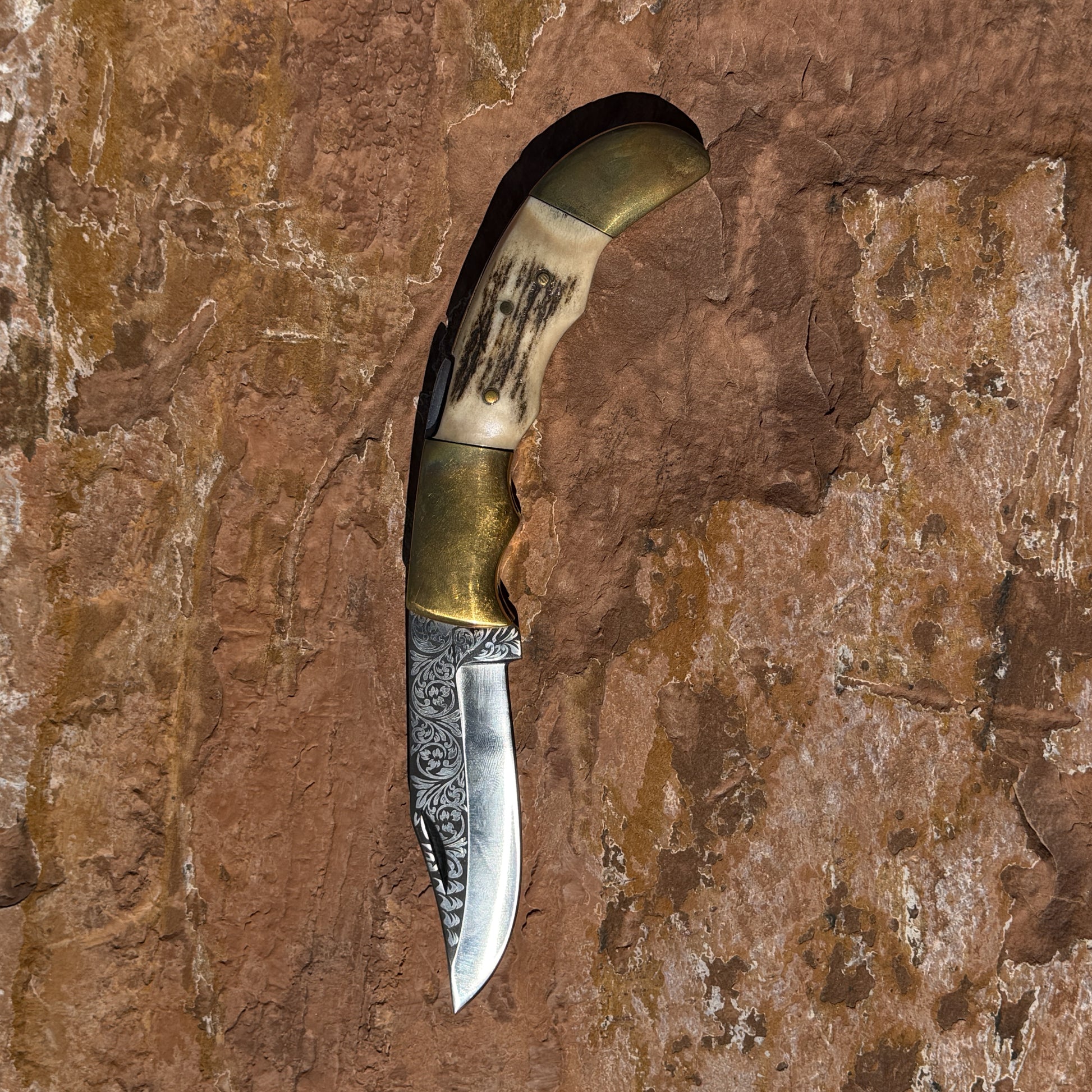 Ironclad Stag Fang Folder 1095 steel folding knife with laser etched blade, stag handle, and brass bolsters displayed on rock background