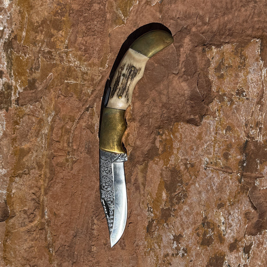 Ironclad Stag Fang Folder 1095 steel folding knife with laser etched blade, stag handle, and brass bolsters displayed on rock background