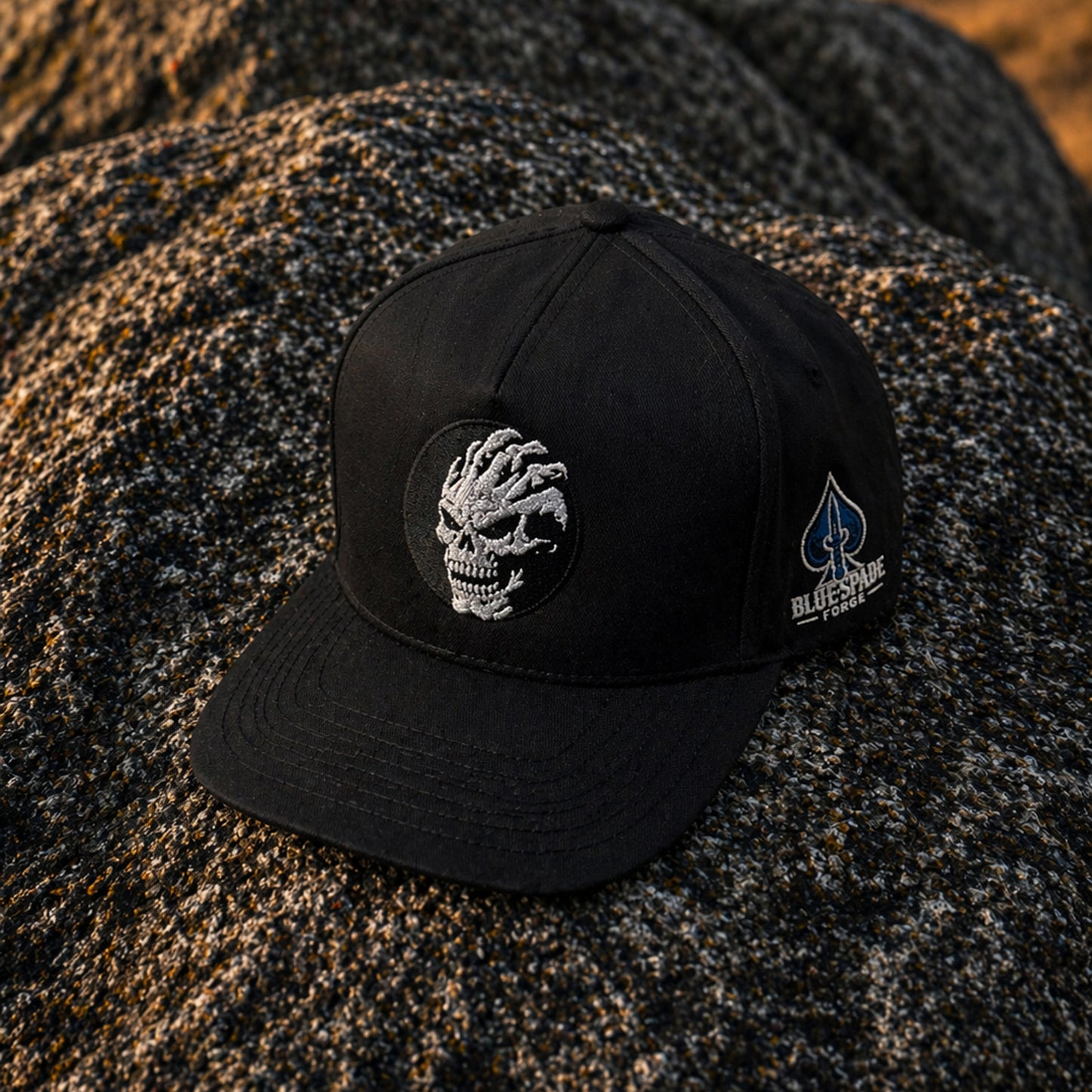 Black Talon Skeleton hat by Blue Spade Forge with skull embroidery and blue spade logo on black Richardson snapback displayed on rock outdoors